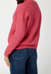 Roze gebreide trui met een ronde halslijn, geribde manchetten en een textuur achter met een kanten patroon, gecombineerd met donkerblauwe jeans.
