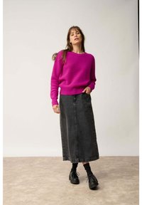 Pull en tricot fuchsia avec un motif texturé, associé à une jupe en denim noire taille haute. Le mannequin porte des chaussures à plateforme noires.