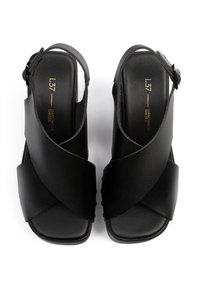 Mustat slingback-kengät, joissa on sileä nahkapinta. Ristiin menevät hihnat edessä ja säädettävä nilkkahihna. Neliömäinen kärki.