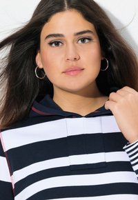Sweat à rayures bleu marine et blanc, avec une capuche à cordon, des accents rouges et un tissu doux. Des boucles d'oreilles rondes complètent le look.