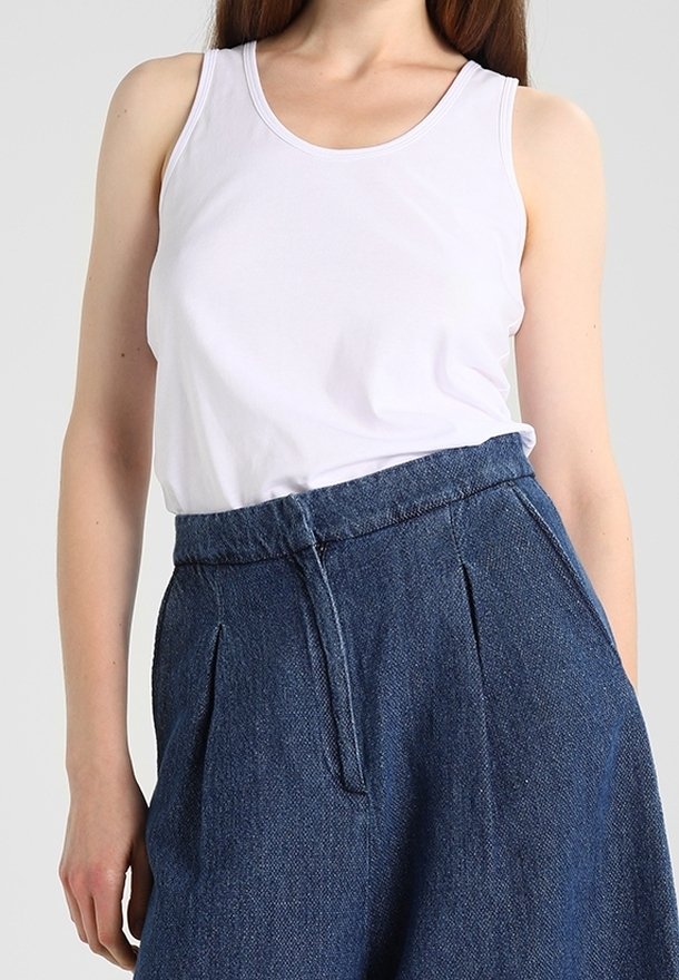 Biała bawełniana koszulka na ramiączkach z okrągłym dekoltem w zestawie z jeansami w kolorze niebieskim o wysokim stanie, posiadającymi zaszewki i teksturowaną tkaninę.