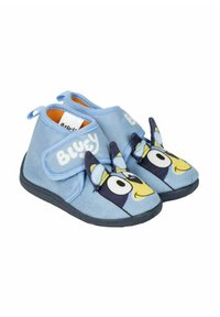 Zapatillas azules hechas de un tejido suave con un diseño de un perro de dibujos animados en azul y amarillo en la puntera. Presentan una tira de velcro y suela de goma.