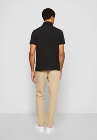 Polo noir à manches courtes avec un col, porté avec un pantalon beige et des baskets blanches. Texture lisse, design ajusté et style simple.