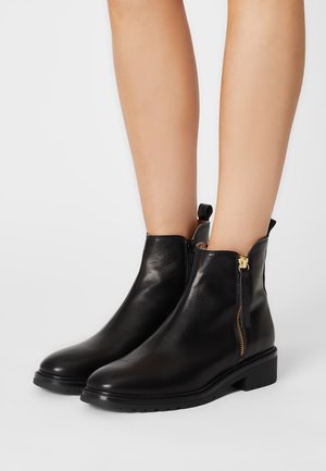 Bottines en cuir noir avec une texture lisse, fermeture éclair sur le côté et un petit talon carré. Elles possèdent une languette à l'arrière pour un enfilage facile.