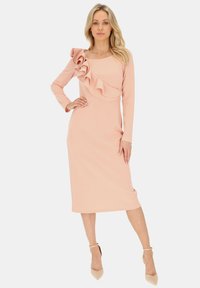 Pudrowo-różowa sukienka z długim rękawem, z falbaniastym akcentem na jednym ramieniu i prostą sylwetką, wykonana z gładkiego materiału.