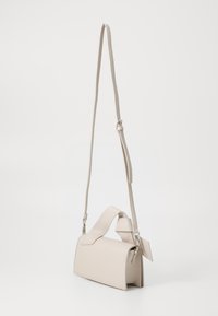 Sac à bandoulière beige clair avec une forme structurée, en cuir lisse, avec une bandoulière ajustable et une accent de tag sur le côté.