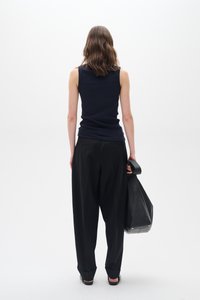 Mornarsko modra rebrasta brezrokavnik s črnimi širokimi hlačami. Model drži črno torbo, stoji ob navadni beli ozadju.