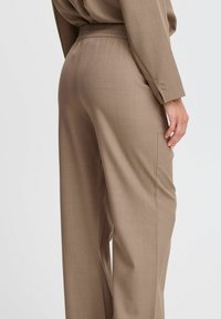 Pantaloni in tessuto di un marrone chiaro, con una consistenza, vita elasticizzata, gamba larga e tasche laterali, caratterizzati da un design liscio e sartoriale.