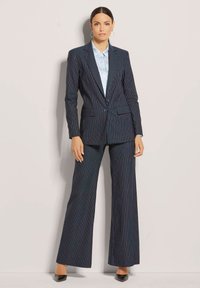 Navyblauer Nadelstreifenanzug mit hellen vertikalen Streifen, bestehend aus einem taillierten Blazer, weitem Hosenbein und einem hellblauen Hemd mit Kragen.