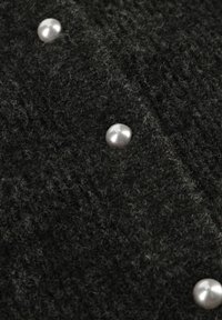 Zwarte gebreide stof met een textuur, voorzien van twee glanzende parelachtige accenten. Het materiaal lijkt zacht en pluizig.