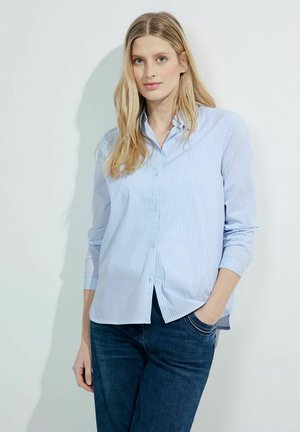 Hellblaues Button-up-Hemd mit vertikalen weißen Streifen, langärmlig und lässig geschnitten. Kombiniert mit dunkelblauen Denim-Jeans.