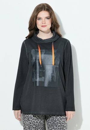 Czarny longsleeve z dekoltem typu cowl, z graficznym nadrukiem i pomarańczowymi sznurkami. W zestawie ze wzorzystymi spodniami w odcieniach szaro-czarnych.
