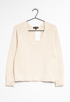 Cremefarbener, gestrickter Pullover mit V-Ausschnitt, gerippten Bündchen und einem strukturierten Muster. Hängt an einem schwarzen Haken vor weißem Hintergrund.