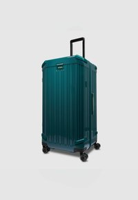 Turkooise harde koffer met verticale groeven, zwarte wielen, een uitschuifbare handgreep en een zijhandgreep voor eenvoudige bediening.