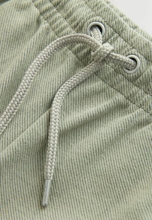 Zöld csíkos szövet, texturált felülettel, fonott húzózsinórral, amely fémfüleken keresztül van átfűzve. Közeli kép.