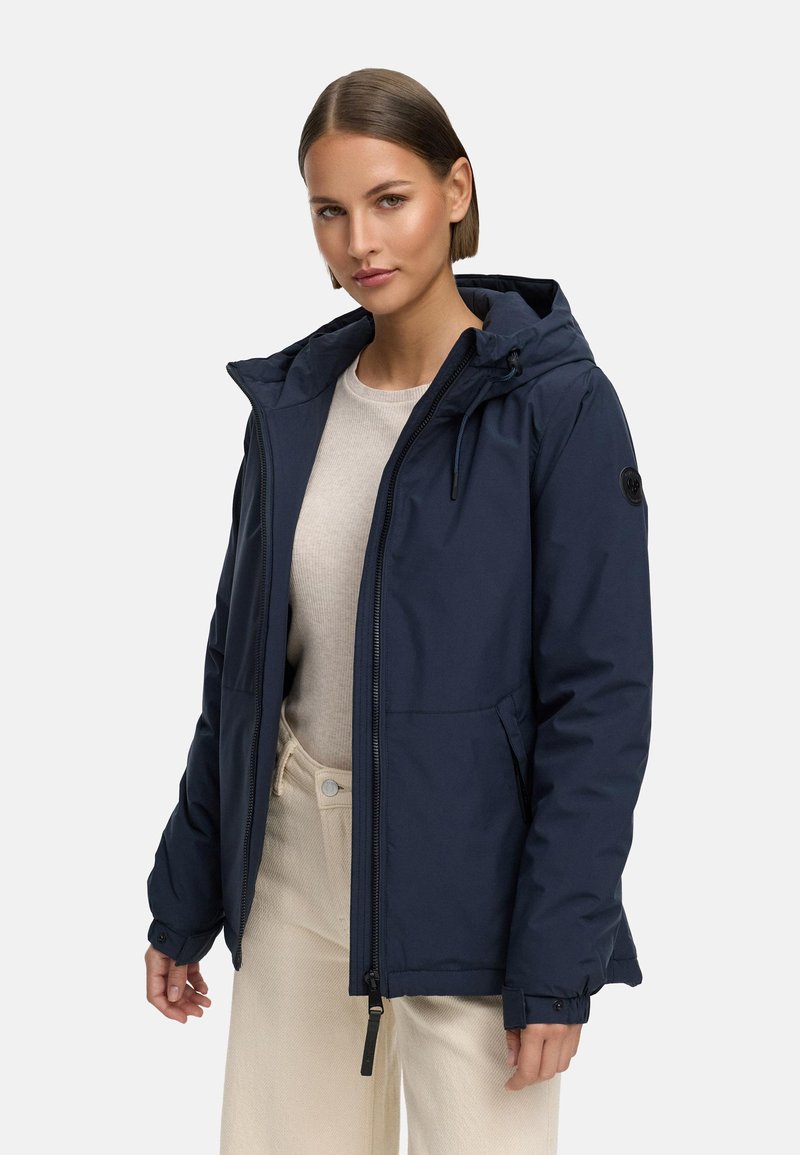 Marinblå vattentät jacka med huva, framzipper och sidofickor. Har en diskret svart logpatch och elastiska ärmslut.