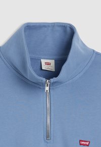 Helles blaues Zip-up Sweatshirt mit hohem Kragen, weichem Stoff und einem roten Levi's-Logo auf der linken unteren Seite.