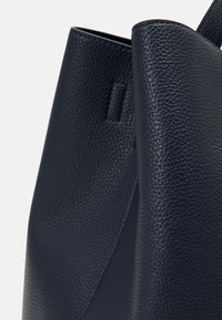 Borsa tote in pelle blu navy con una finitura texture e un bordo liscio, caratterizzata da un design minimalista e un delicato accento laterale.