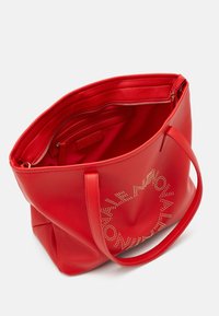 Red leather tote bag with a textured finish, featuring two shoulder straps and a zippered pocket inside. Gold accents in a circular pattern.
