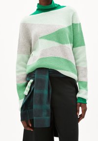 Pull en maille rayé vert et gris, avec une coupe décontractée, une texture côtelée et un col roulé superposé vert. Porté avec un pantalon à carreaux.