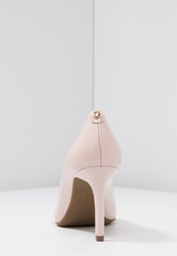 Escarpin en cuir verni rose doux avec un bout pointu. Présente un accent décoratif doré au talon. Talon aiguille effilé et élégant.