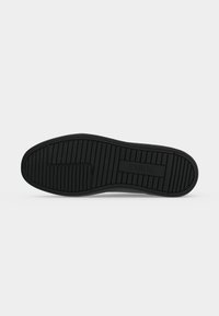 Semelle de chaussure en caoutchouc noir avec des rainures horizontales et verticales, avec le mot « GUESS » embossé dans le rectangle central.