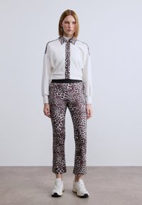 Λευκό φούτερ με λεπτομέρειες σε λεοπάρ σχέδιο, σε συνδυασμό με εφαρμοστά παντελόνια με λεοπάρ μοτίβο. Διαθέτει γιακά, ριμπ μανσέτες και μαύρη ζώνη στη μέση.