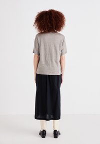 Szürke, rövid ujjú póló, amelyet fekete szoknyával párosítottak, laza szabással és puha anyagból készült. Az outfit fekete cipőkkel van kiegészítve.