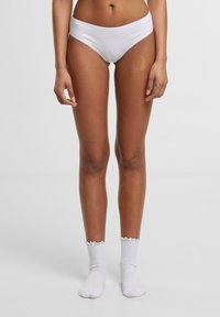 Bijele pamučne bikini gaćice s glatkom površinom, u kombinaciji s bijelim rebrastim čarapama s valovitim rubom.
