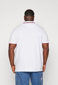 White polo shirt with red accents on the collar and sleeve cuffs, featuring a relaxed fit and soft cotton material. Rear view displayed.
