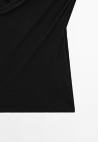 Sort, ribbet stof hænger blødt; det har en buet kant og en glat tekstur, hvilket skaber en afslappet silhuet.