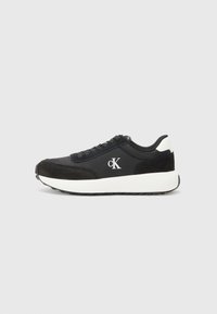 Zwarte sneaker met een mix van glad textiel en suede materialen, witte tussenzool en een logo in contrasterend wit op de zijkant.