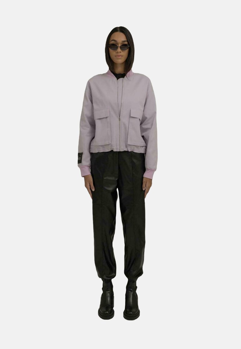Lys lilla cropped jakke med to frontlommer, sammen med svarte, løse bukser og svarte ankelstøvler. Modell som har på seg svarte solbriller.