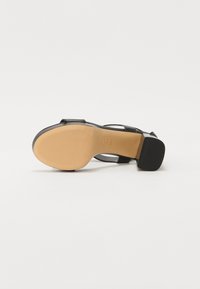 Sandale noire avec semelle texturée couleur fauve et petit talon bloc, vue du côté de la semelle sur fond blanc.