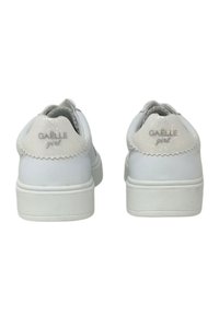 Sneakers bianchi con esterno in pelle liscia, forma arrotondata e dettagli a onde sul tallone. Presentano il logo "GAËLLE girl" in argento.