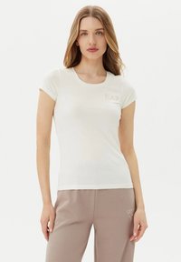 T-shirt bianca aderente in morbido cotone, con scollatura rotonda e maniche corte, arricchita da un piccolo logo EA7 in dettagli chiari sul petto.