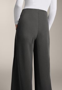 Široké tmavosivé nohavice s vertikálnou ribovanou textúrou, s bočnými vreckami a vysokým pásom pre uvoľnený strih.