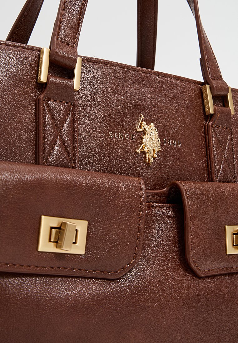 Sac à main en cuir marron avec quincaillerie dorée, logo embossé et poche à rabat avec fermeture à clasp, présentant une finition texturée et un design structuré.