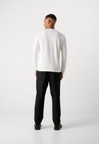 Tricou alb cu mâneci lungi și guler rotund, combinat cu pantaloni negri. Ținuta are o croială lejeră și o textură fină.