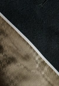 Schwarzes Filzmaterial mit einem strukturierten goldenen Stoff darunter, getrennt durch einen schmalen weißen Streifen, der einen diagonalen Kontrast schafft.