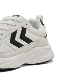 Biały sneaker z czarnymi paskami w kształcie litery V, panelami z siateczki i zamszu, grubą amortyzowaną podeszwą oraz białymi sznurowadłami.