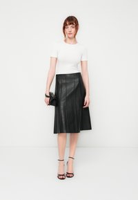 Black pleated leather skirt, knee-length, paired with a fitted white short-sleeve top. Accessorized with a small black handbag and strappy heels.