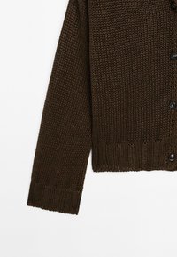 Cardigan en maille marron avec un motif texturé, des poignets et un ourlet côte à côte, et des boutons noirs sur le devant.