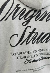 Hallilasehall, kus on mustade cursive ja serif fontide tekstiga hall dress. Olulised detailid hõlmavad printimist, mis ütleb "Asutatud üheksateist...".