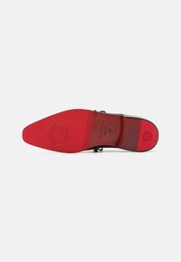 Scarpa in pelle nera con una finitura lucida, dotata di punta affusolata e suola rossa vivace. Dettaglio del logo impresso sulla suola.