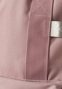 Roze stoffen tas met een gestructureerd oppervlak, stevige geweven riem en een klein metalen label met een logo.