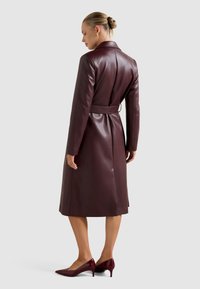 Μπορντό δερμάτινο παλτό τύπου trench με ζώνη στη μέση, μακριά μανίκια και κλασικό γιακά. Λείο υλικό με μήκος που φτάνει μέχρι το γόνατο.