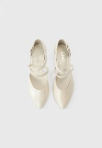 Μπεζ δερμάτινα γοβάκια με ψηλό τακούνι και μυτερές μύτες, με σταυρωτούς ιμάντες και διακοσμητική αγκράφα. Λείο, γυαλιστερό φινίρισμα.