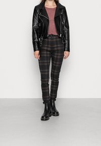 Schwarze Lederbikerjacke mit silbernen Beschlägen, kombiniert mit taillierten Karo-Hosen und schwarzen Knöchelboots. Das Oberteil ist ein strukturierter rosafarbener Pullover.