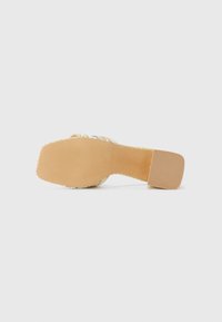 Sandal med hæl og flettet overdel i beige og gulltoner. Firkantet hæl og teksturert såle for godt grep. Enkel design, lett materiale.